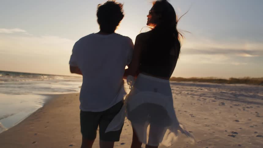 Young couple walking on the beach holding hands and putting their arms around each other