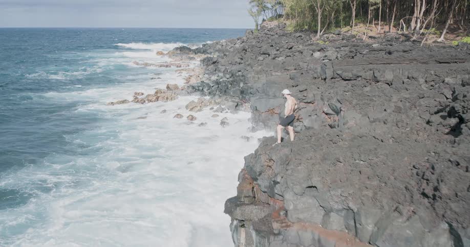 Man standing on volcanic rocks at the edge of the rough sea