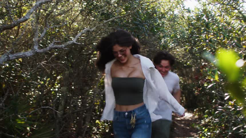 Young couple hold hands as they run on a trail through the woods