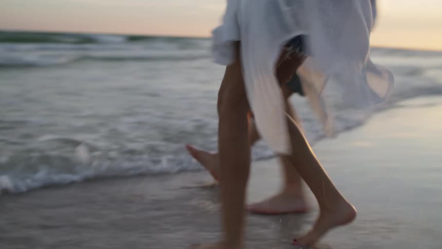 People walking barefoot by the sea at sunset