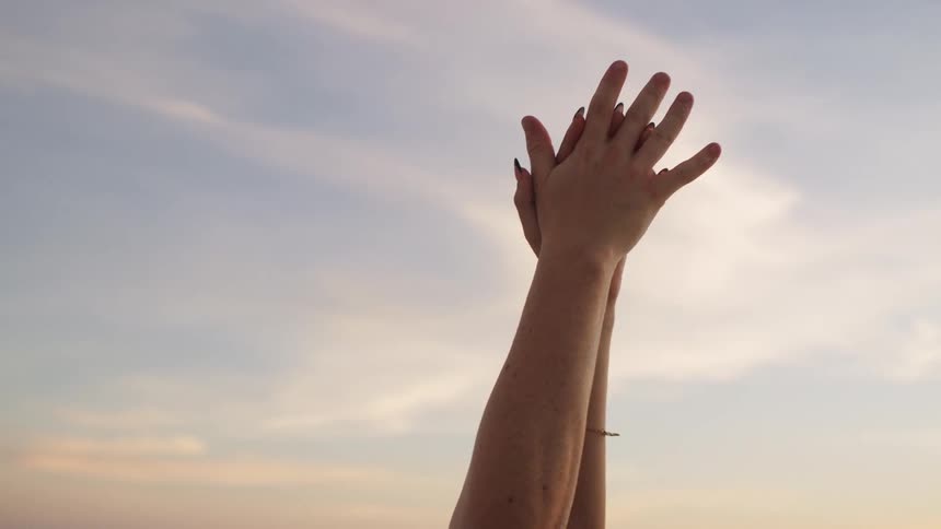 Pair of hands clasped together against a cloudy late afternoon sky