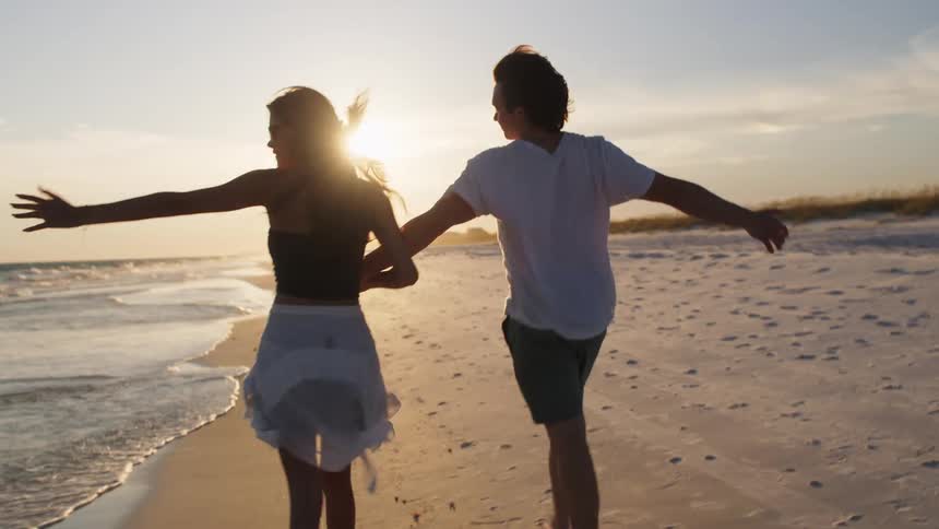 A couple hold hands while walking on the beach