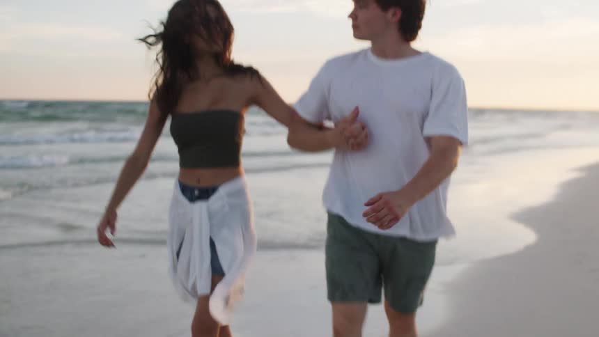 Young couple hold hands as they walk along the beach