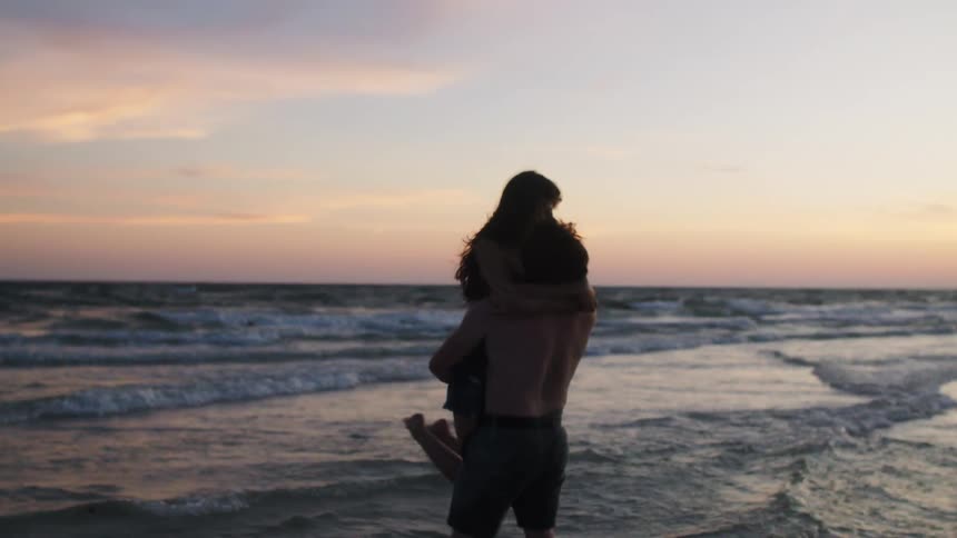 Man holding a woman in his arms by the seaside at sunset