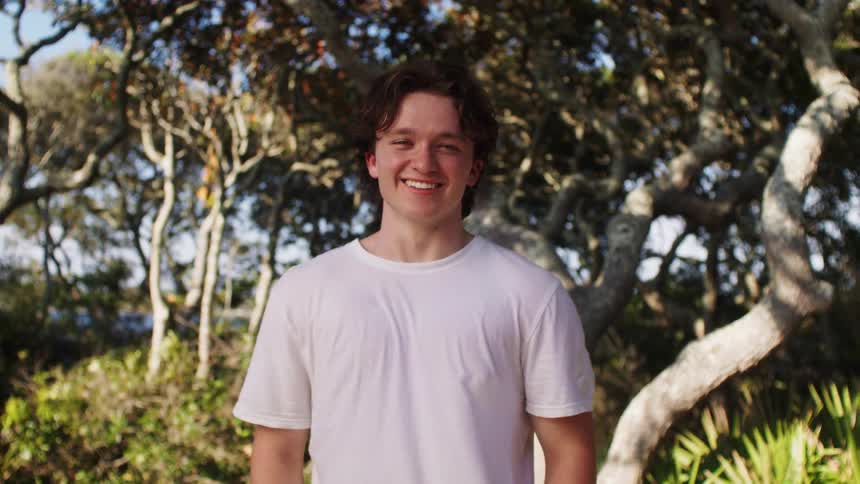 The teenager is outside smiling by the trees