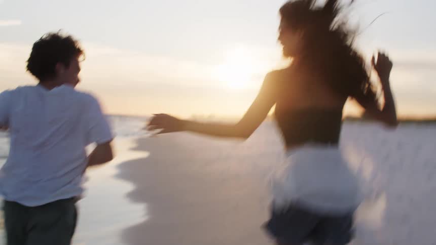 A couple holds hands while running on the beach at sunset