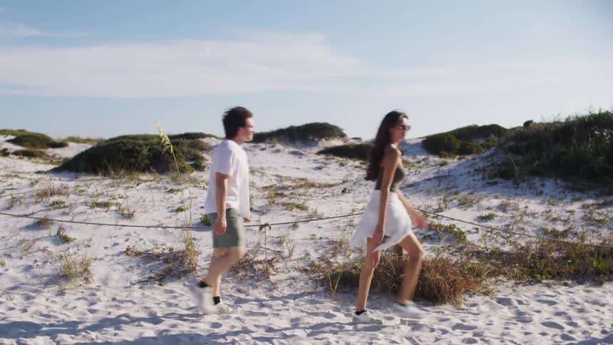Man and woman walking together along a sandy trail between dunes