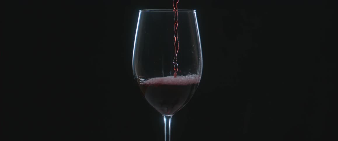 A glass being filled with red colored liquid in a dark area