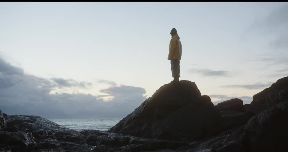 Woman stands on a rock along the coast as waves splash into shore