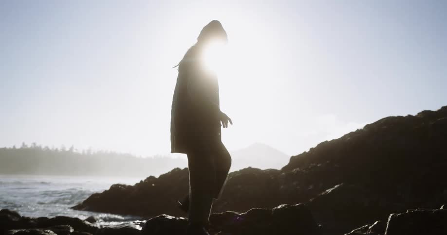 Person walking on rocks by the sea wearing a beanie and coat