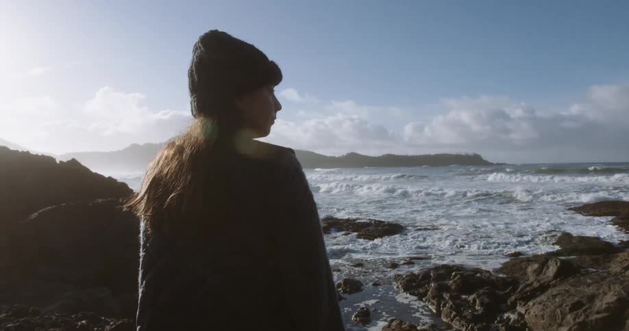 Young woman standing on rocks along the coast as waves roll into shore