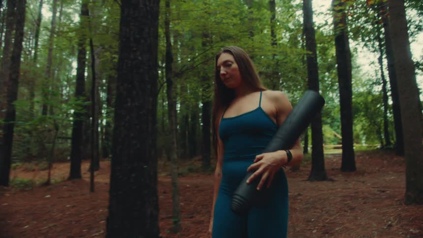 Woman walking along a forest trail in blue sportswear and a yoga mat