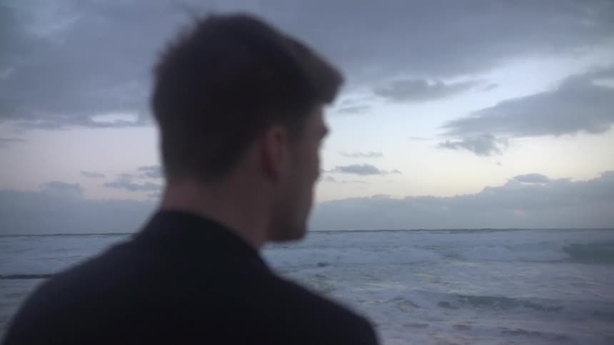 A man stands near the water on a cloudy day