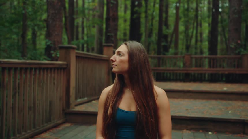 Woman sitting with eyes closed on a wooden deck surrounded by forest