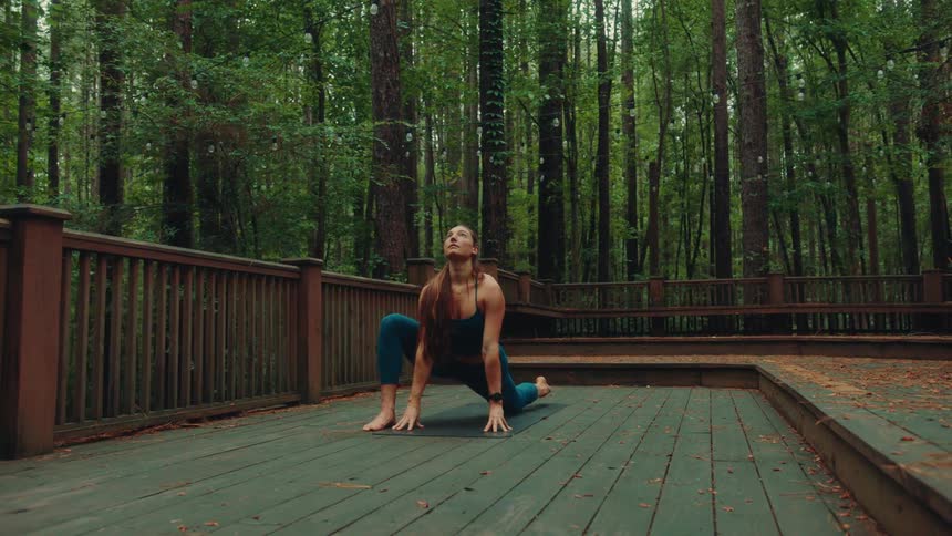 Female doing yoga on a balcony surrounded by trees in the forest