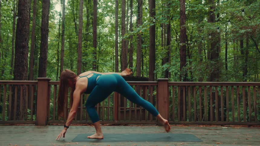 A woman performs stretching exercises outdoors on a wooden deck