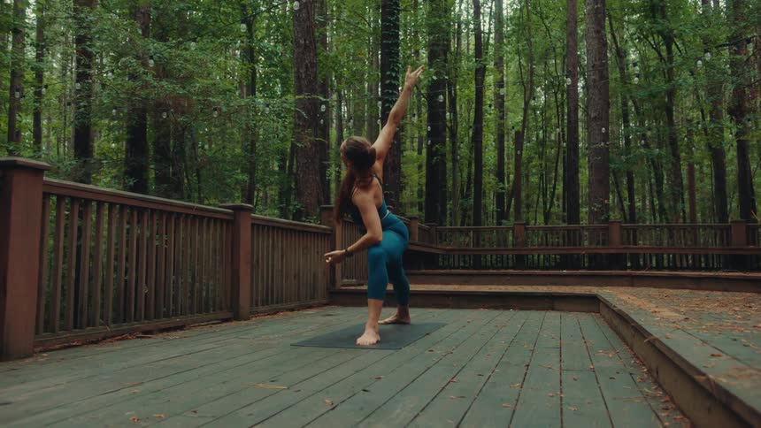 A woman does yoga stretches on a deck surrounded by forest