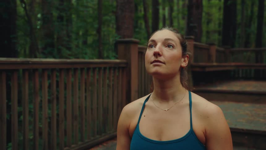 A woman is outdoors on a patio in a forest while looking upwards