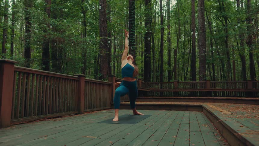 A young woman stretches outdoors on a wooden deck in a forest