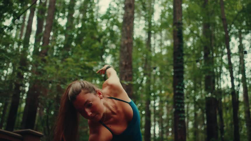 A young woman performs yoga stretches on a wooden deck in an evergreen forest