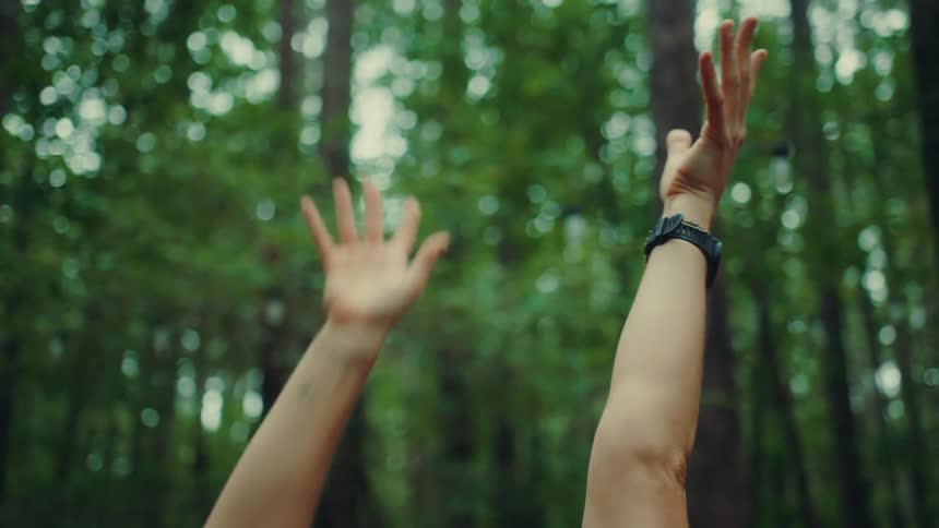 A female is stretching her arms up in the woods