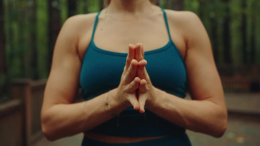 A woman doing yoga outdoors in the woods at midday wearing a blue shirt