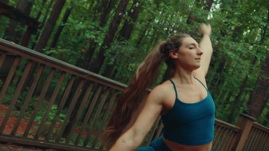 A woman practices yoga while outdoors surrounded by tall trees