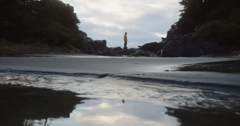 Woman walks on rocks along the coast as water flows in the river