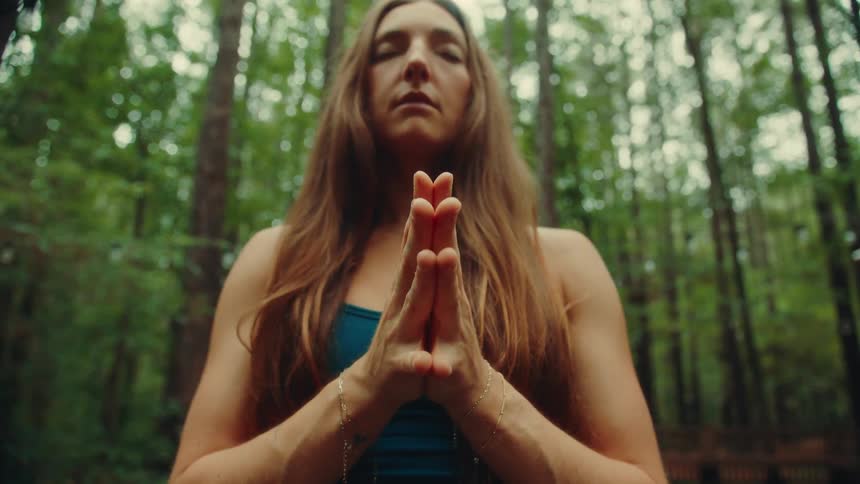 A woman with long hair meditates while outside in a forested area