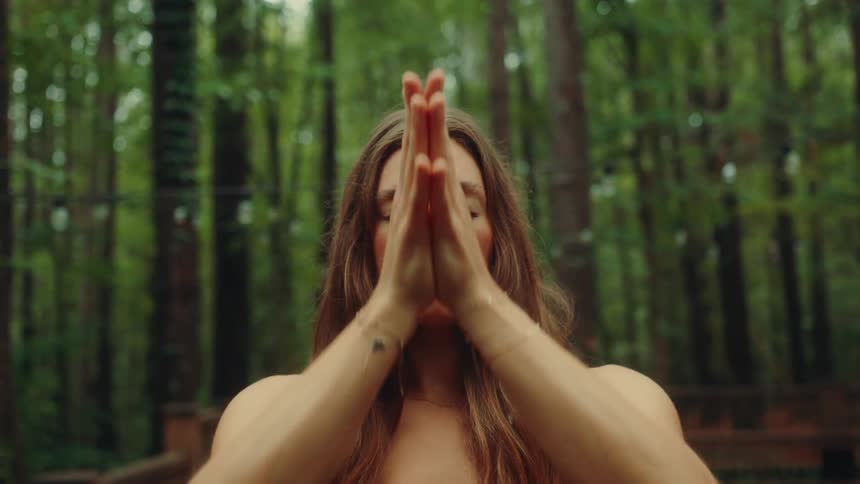 A woman brings her hands together while meditating outddors
