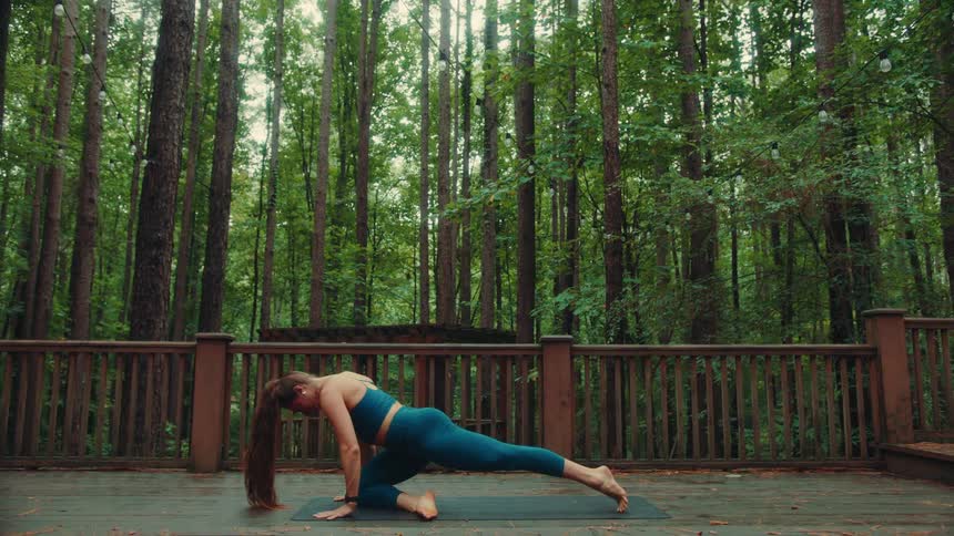 Female doing yoga on a balcony surrounded by trees in the forest