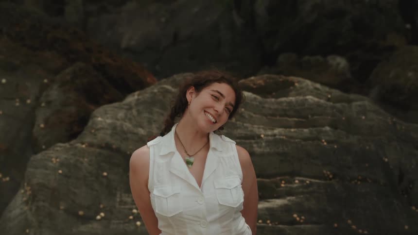 A young woman adjusts her pigtails as she smiles and poses for a photo in front of a rock