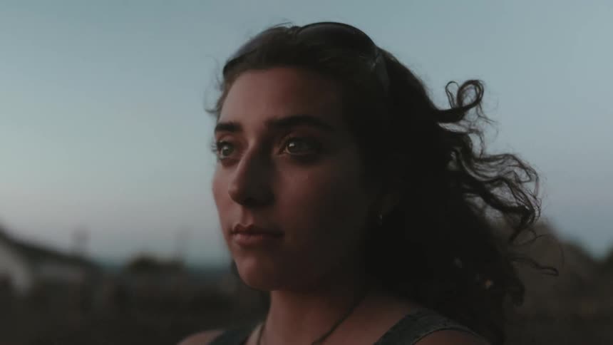 Woman with neutral expression outdoors in late afternoon