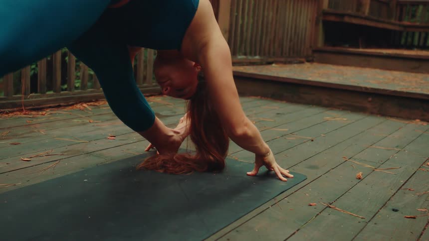 A woman is doing yoga on the wooden boards of the deck