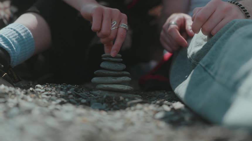 Two people balancing small stones on a stack