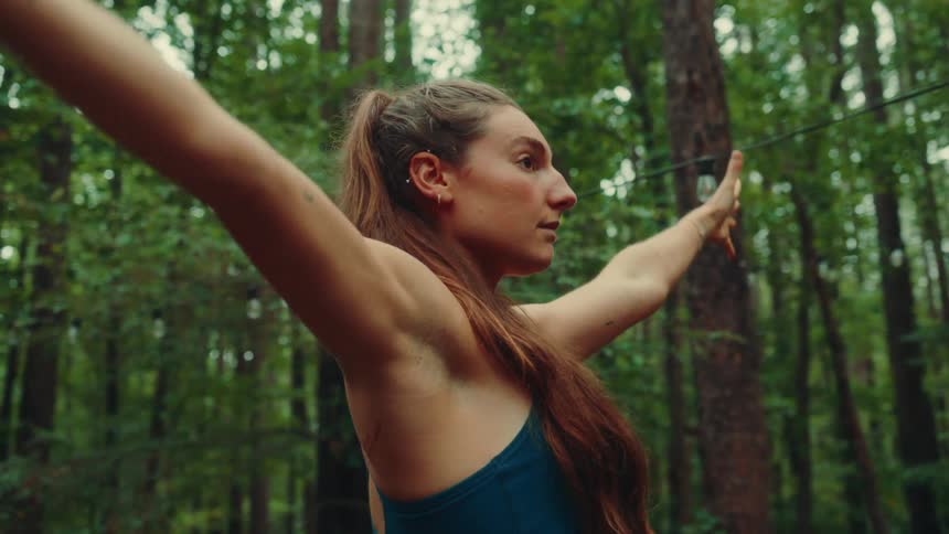 A woman does yoga while outdoors surrounded by tall trees