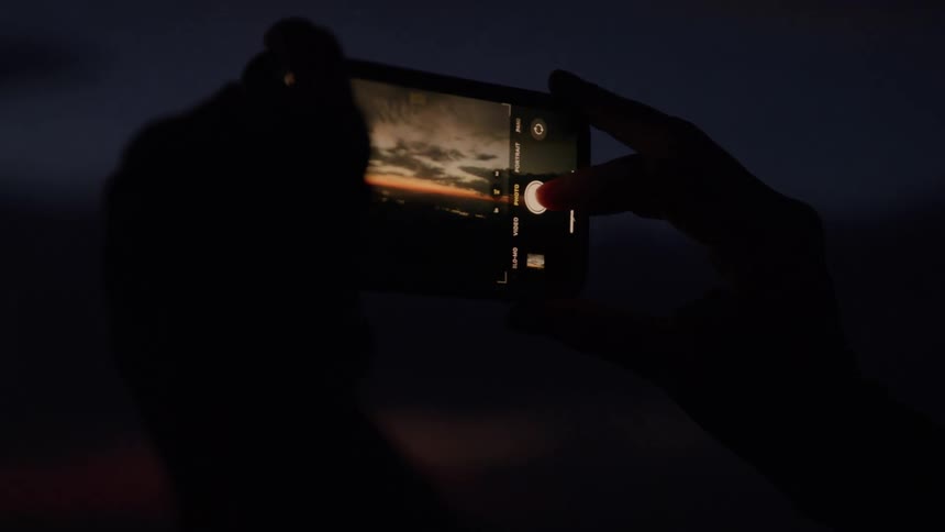 A person looks at a photo of a sunset captured via smartphone