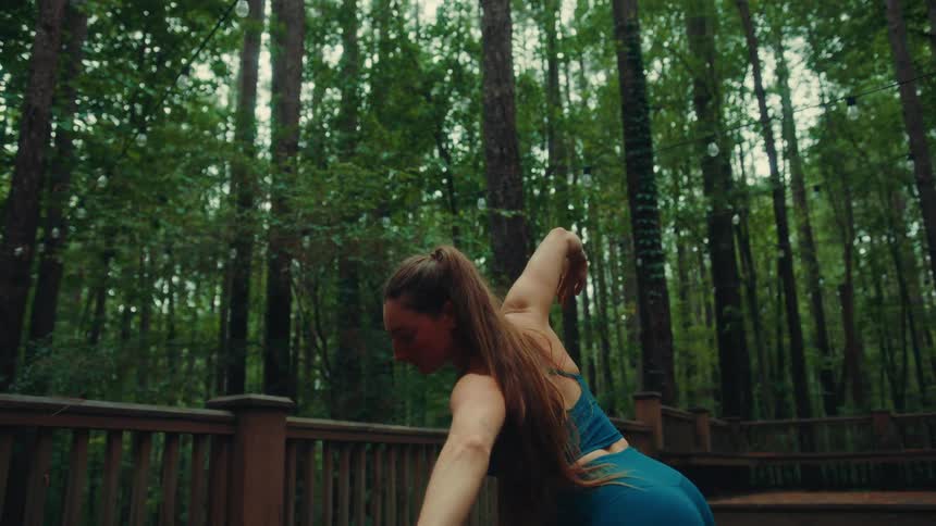 Woman in blue sportswear doing stretching and yoga moves on a wooden deck in the forest