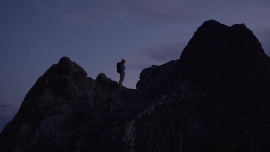 A man stands atop some tall rocks