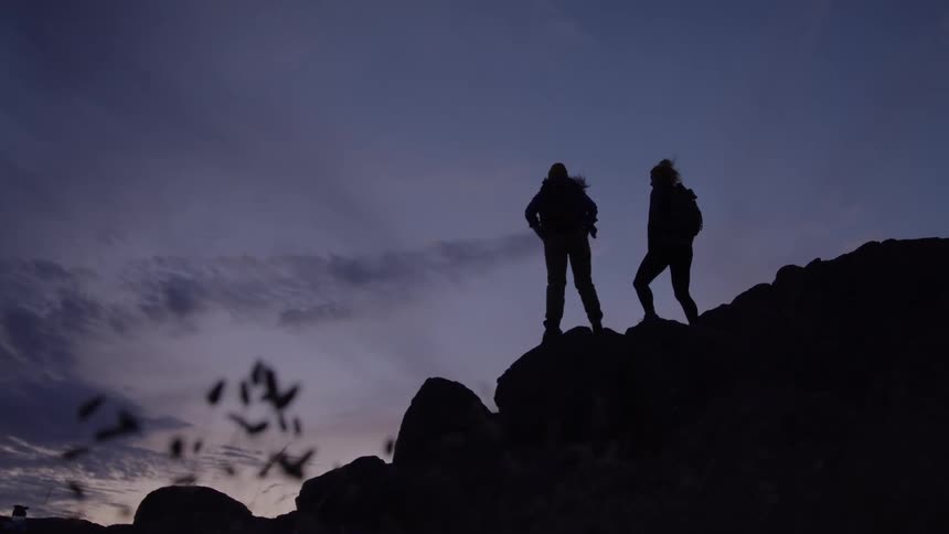 Two people helping each other up a rock and clapping their palms together
