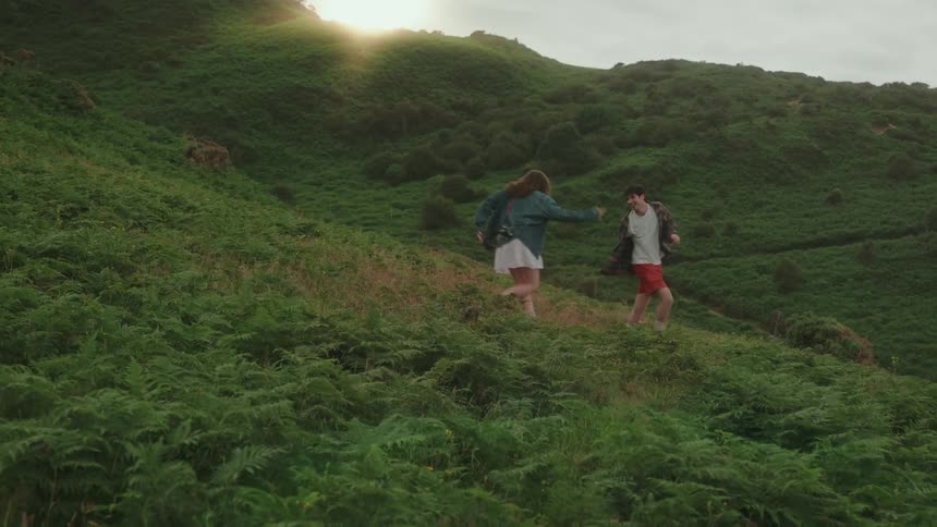 Couple spinning hand in hand in a green field at sunset