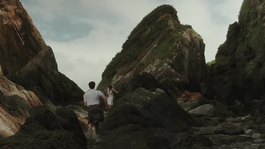 Two people playing hide and seek between tall rocky formations by the seaside