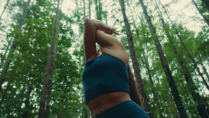 A woman does some stretches while outdoors in the forest