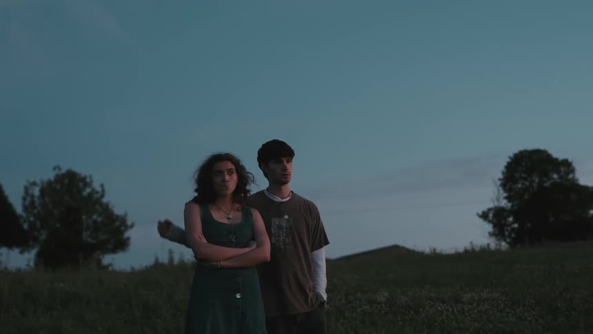 Man placing his hand on the shoulder of a woman next to him in a field in the late afternoon