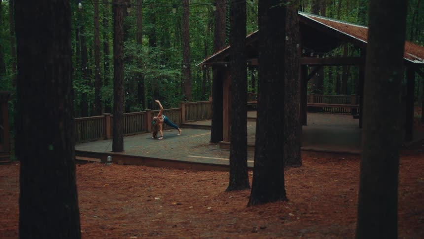A woman doing yoga in a public park surrounded by trees at midday