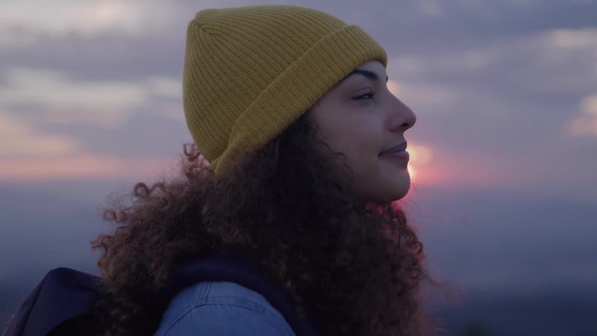 A woman with curly hair smiles while pausing during a hike outdoors
