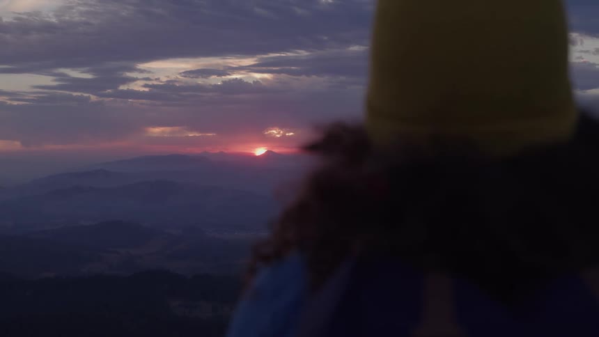A woman watching the sun rising over a mountain range