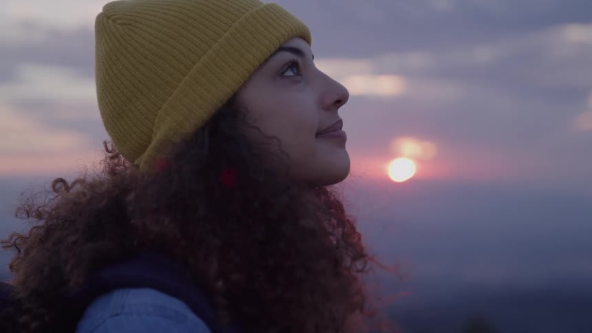 A woman with very curly hair looks upwards and smiles while outdoors