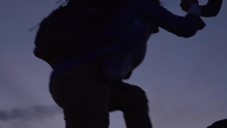 A woman gives another woman a hand to help her climb up a rock during a hike in the wilderness at sunset