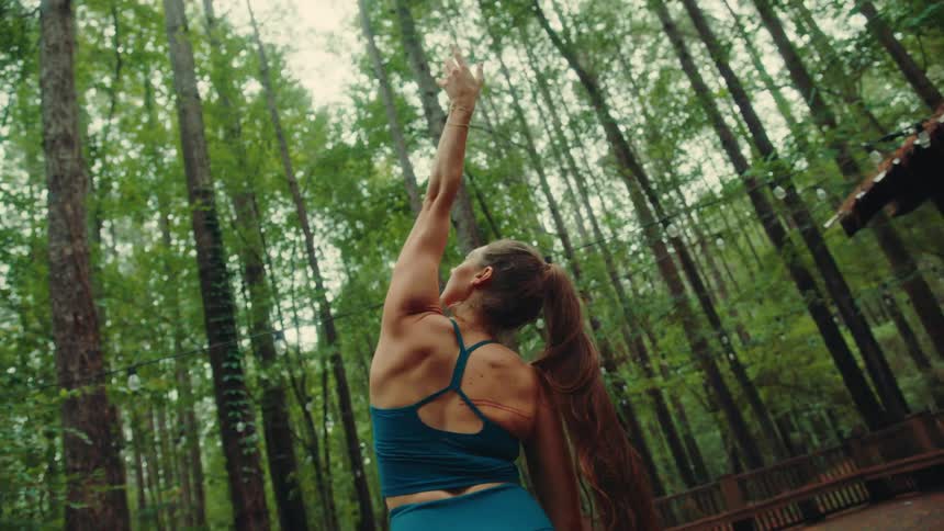 Woman in blue sportswear outdoors surrounded by dense forest doing yoga